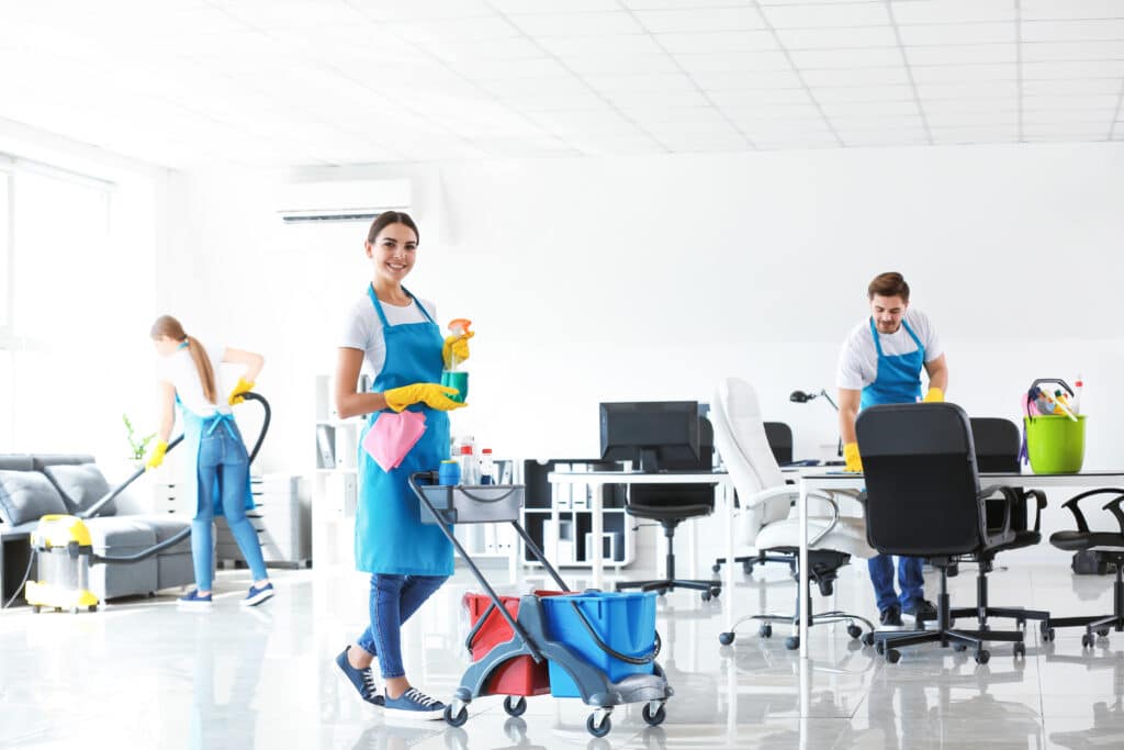 Commercial cleaner with a mop, another pushing a cart of buckets, and a third woman vacuuming a living room, all focused on maintaining cleanliness.