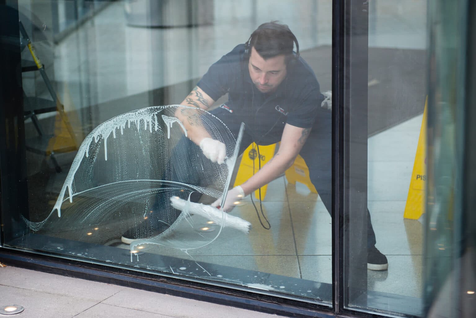 Corporate cleaner using headphones to clean glass door with cloth