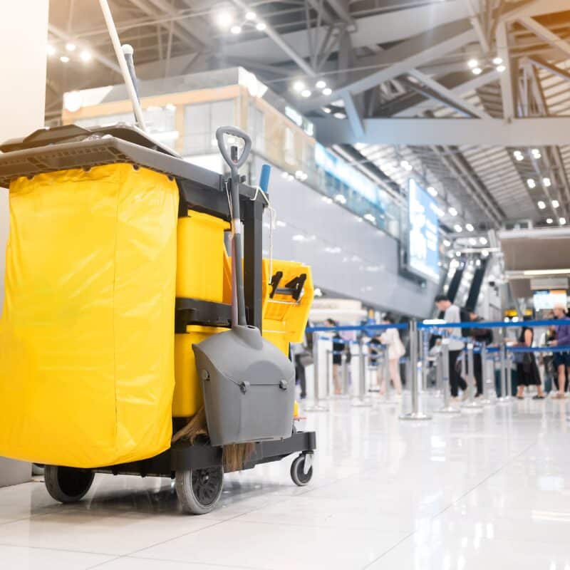 A yellow cleaning cart with a black bag is located in an airport. It is ready for cleaning and maintenance tasks.