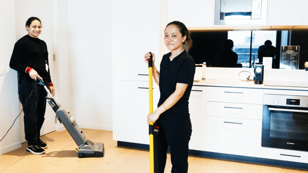 Two women efficiently vacuuming a hotel kitchen, ensuring a clean and tidy environment for guests and staff.