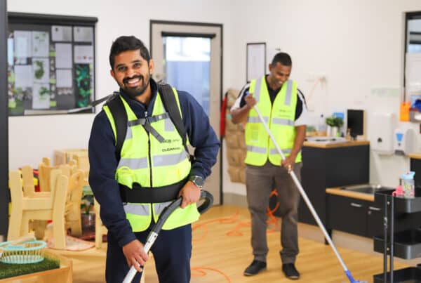 Two men in bright yellow vests are actively cleaning a room, contributing to a neat and well-maintained space.