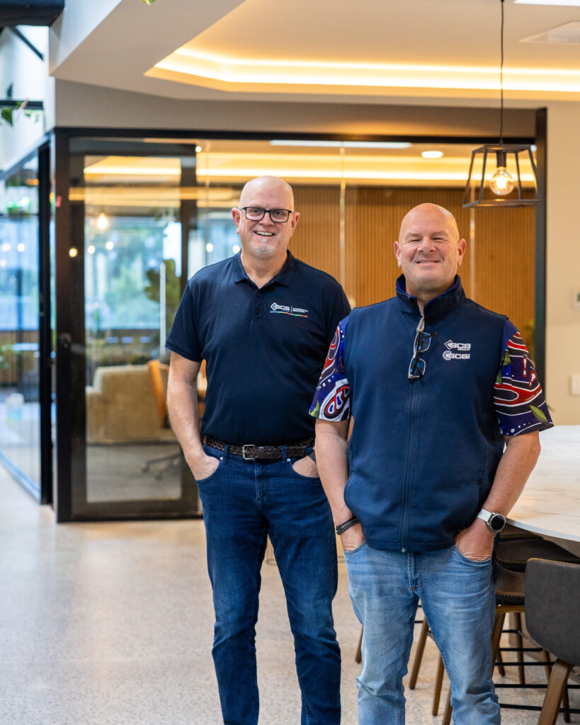 Nick and Glyn from SCS Group standing together in the new office foyer, wearing SCS Group branded shirts with Indigenous-inspired artwork.